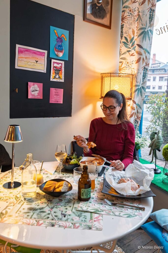 Marie-Caroline déjeunant dans un restaurant à Châlons-en-Champagne avec des plats en papillote et des dessins au mur.