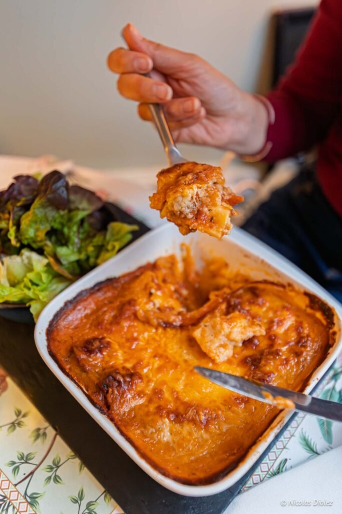 Main tenant prélevant une portion de lasagnes gratinées avec une fourchette, accompagnée d'une salade verte.