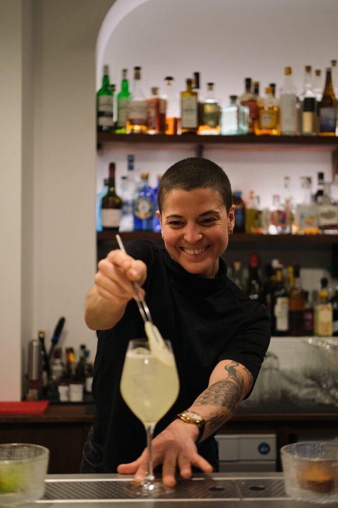 Elsa Leblanc, barmaid souriante, prépare un cocktail derrière le bar pour la Journée internationale des droits des femmes.