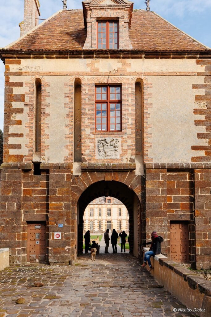 Entrée en pierre et brique du Château de la Rivière avec visiteurs dans l'arche.