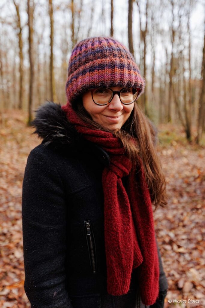 Femme souriante en bonnet coloré et écharpe rouge se promenant dans le parc du Château.