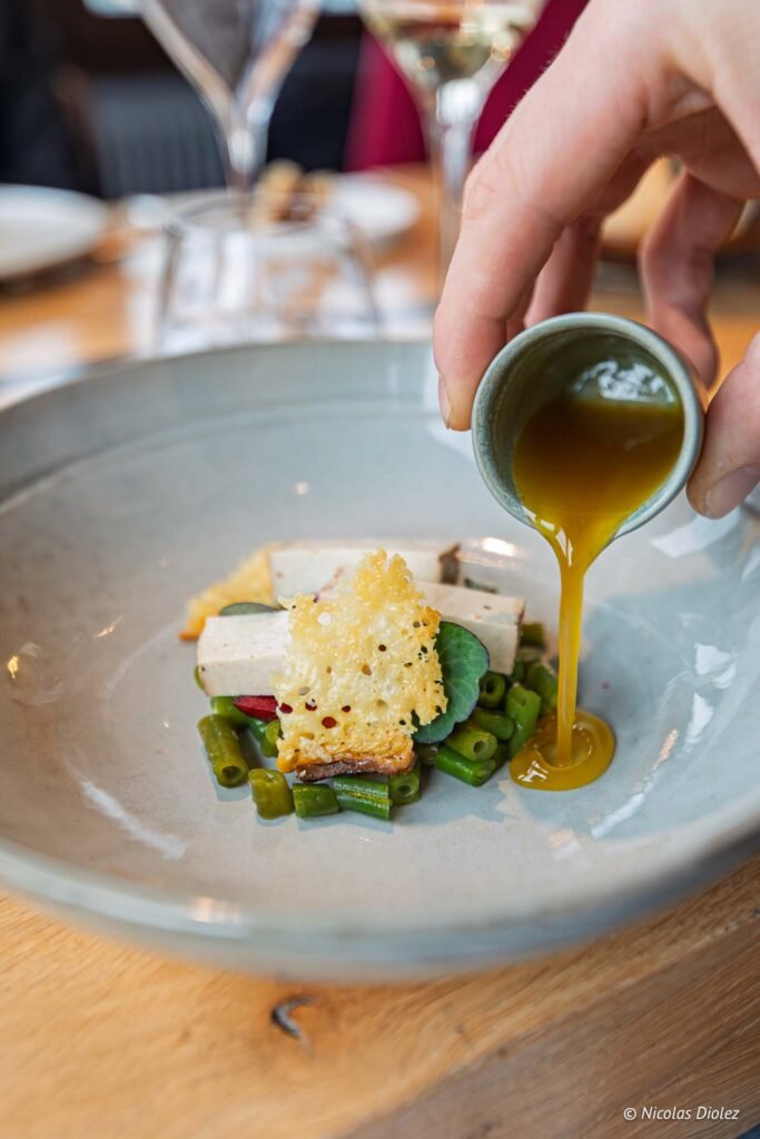 Service d'une sauce gastronomique sur une assiette composée de légumes et de tuile croustillante, restaurant Aux Armes de Champagne.