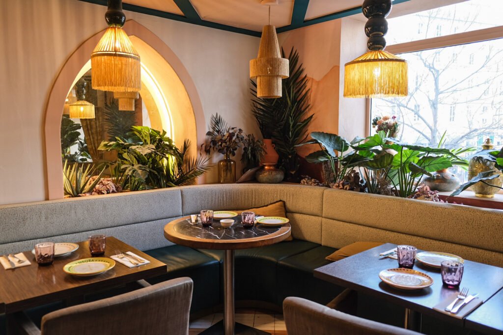 Interior of Noura Opéra restaurant with bench seats, set tables, and plant decor in a warm atmosphere.