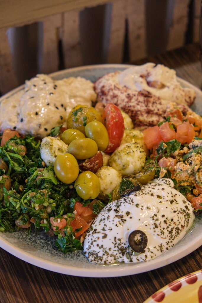 Plate of Lebanese brunch at Noura with tabbouleh, olives, labneh, hummus, and fresh salad.