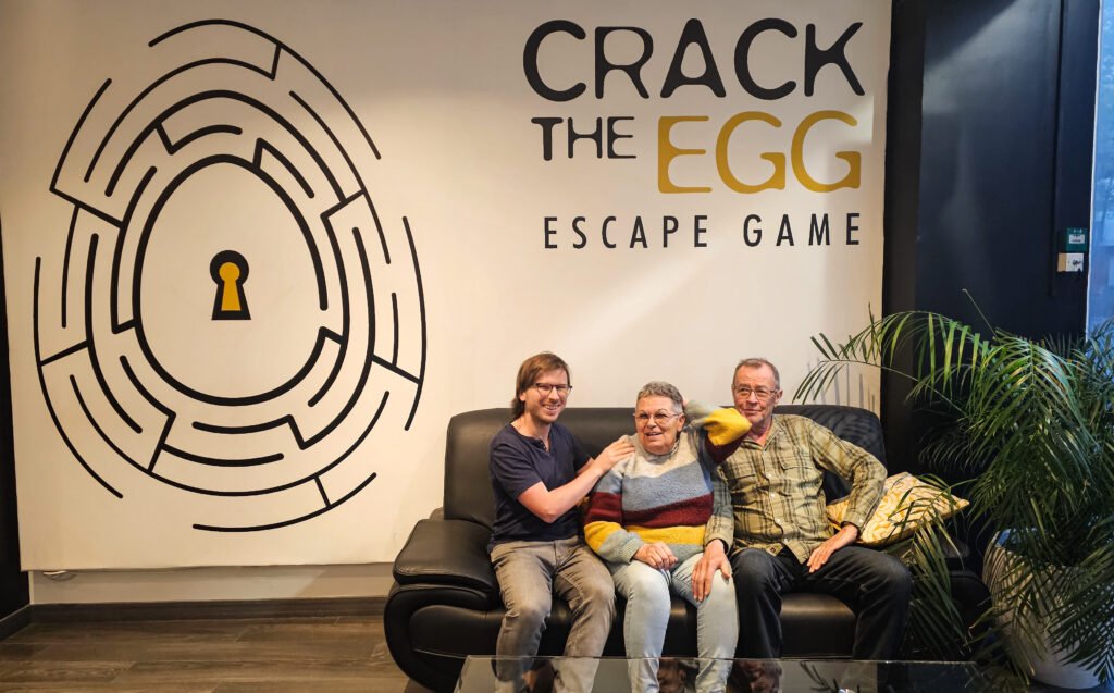 Trois personnes posent sur un canapé noir devant le logo de l'escape game Crack the Egg.