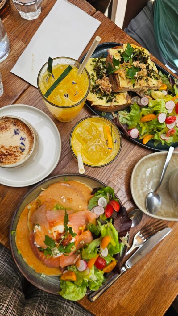 Assiettes de brunch avec saumon fumé, tartines, salade composée et verres de jus frais sur une table en bois.