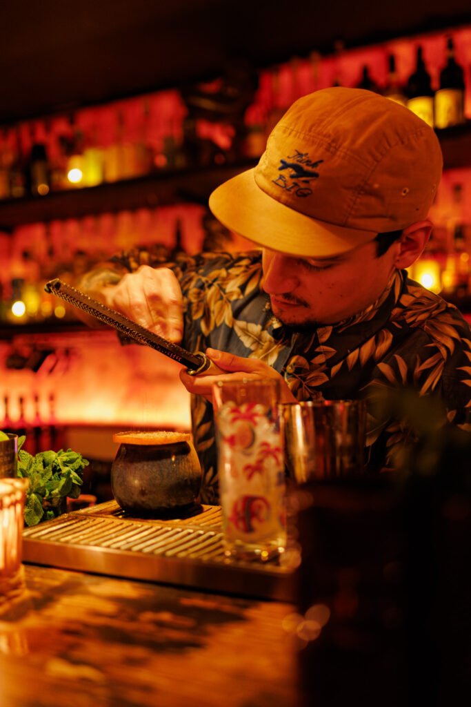 Bartender râpant des épices sur un cocktail Tiki dans un bar à l'ambiance tamisée à Paris.