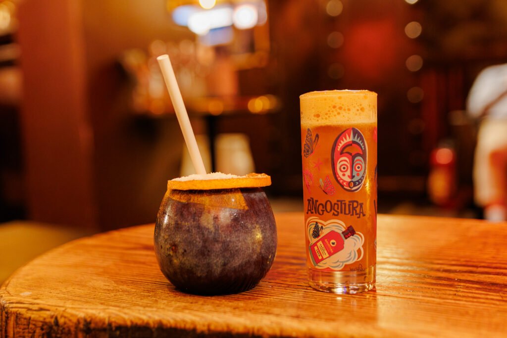 Cocktails tiki, dont un verre décoré Angostura, sur une table en bois au Dirty Dick Paris.