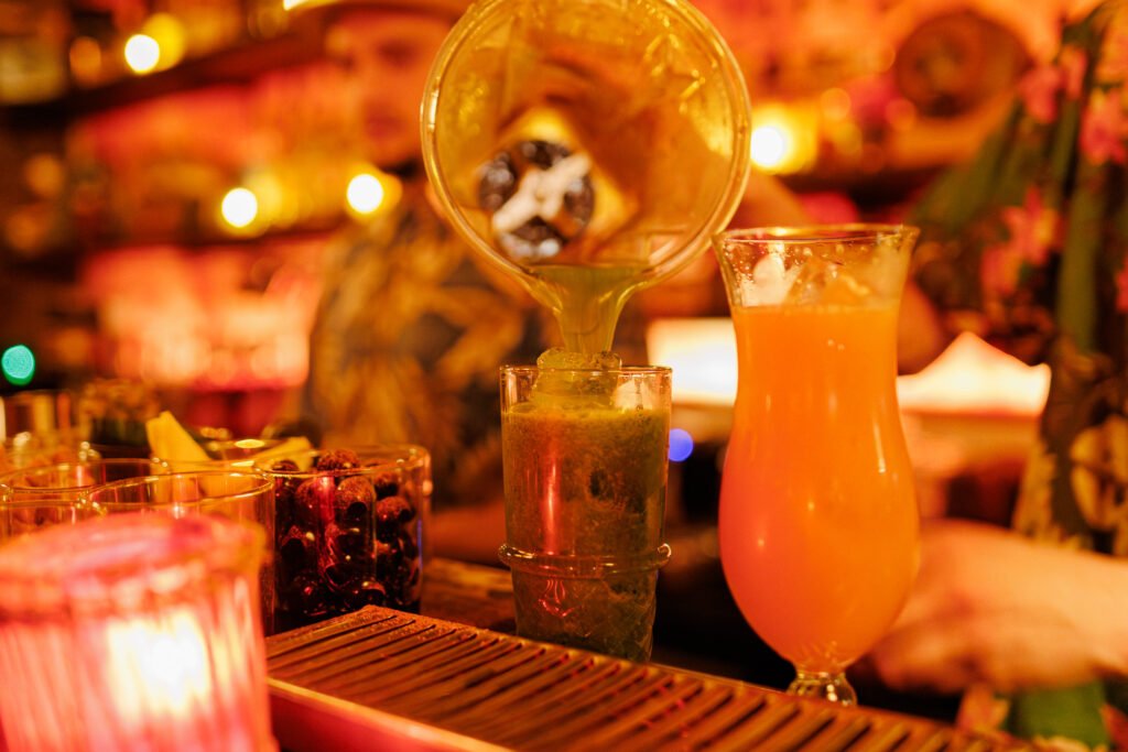 Barman versant un cocktail tiki vert dans un verre rempli de glaçons au Dirty Dick à Paris.