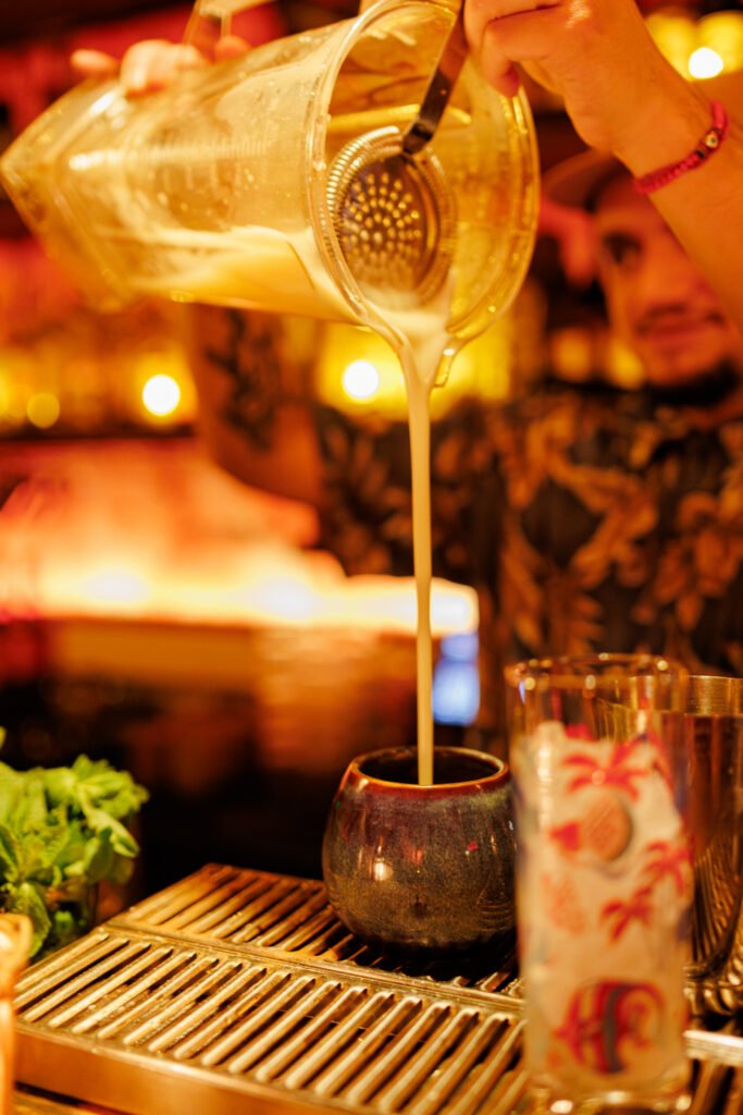 Barman versant un cocktail tiki dans un mug en céramique au bar Dirty Dick à Paris.