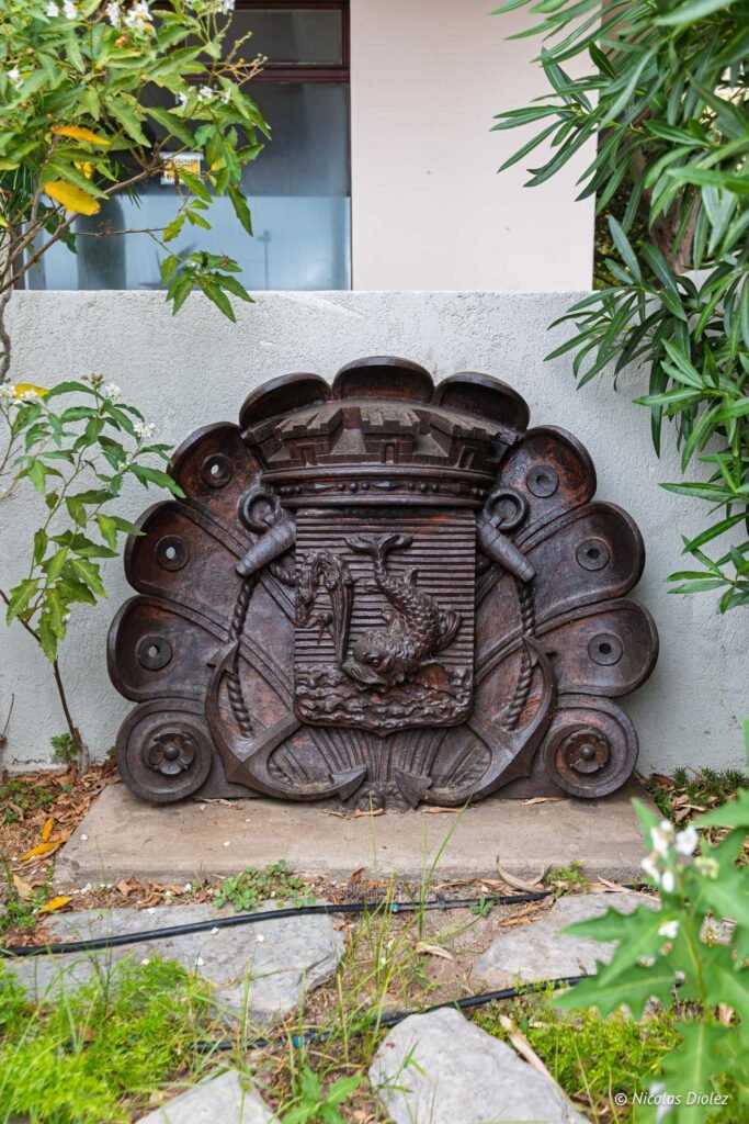 Blason en fonte représentant un dauphin et des ancres marines exposé à l'Espace Paul Valéry.