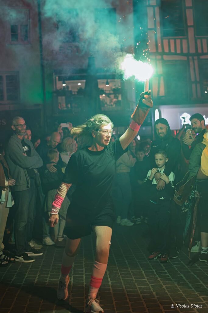 Artiste tenant un fumigène lors de la parade des Furies à Châlons-en-Champagne, devant une foule attentive.