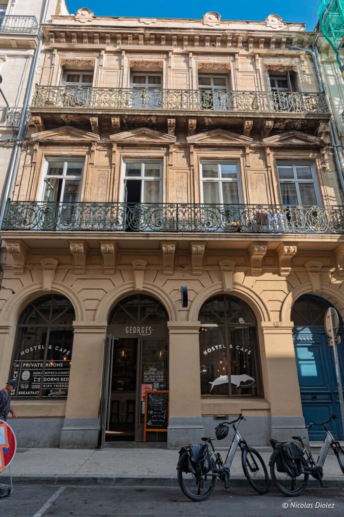 Façade du Georges Hostel & Café à Sète avec ses balcons en fer forgé et vélos garés devant.