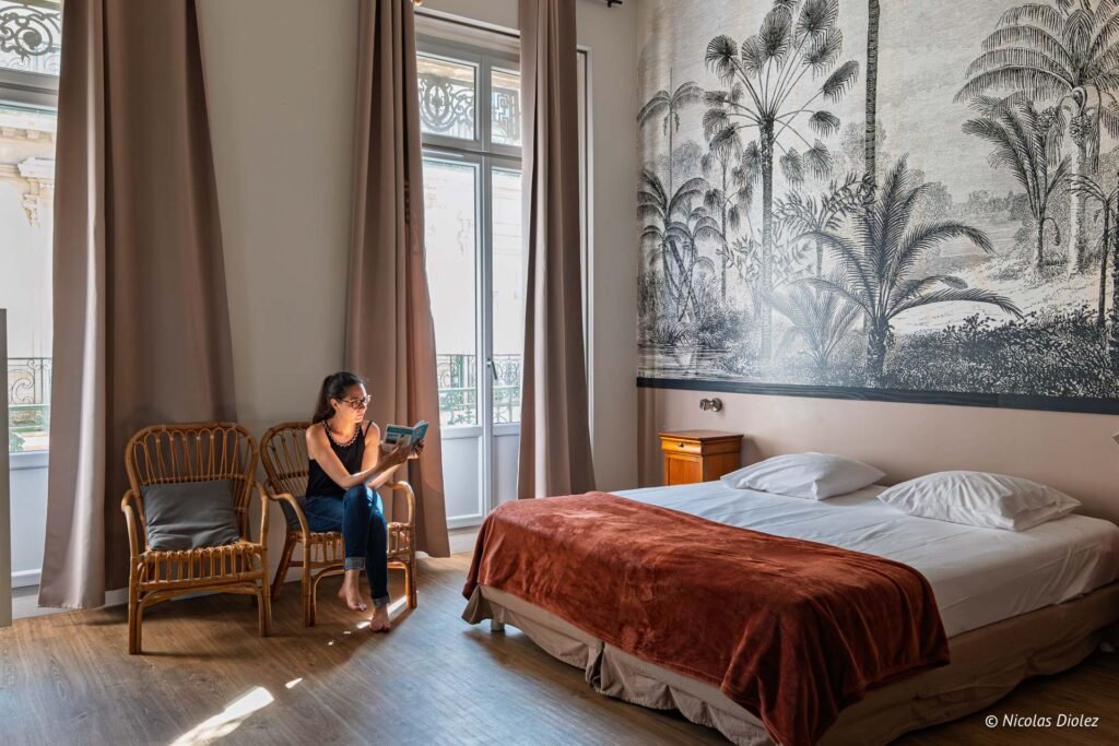 Femme lisant un livre dans une chambre élégante au Georges Hostel à Sète avec papier peint panoramique.