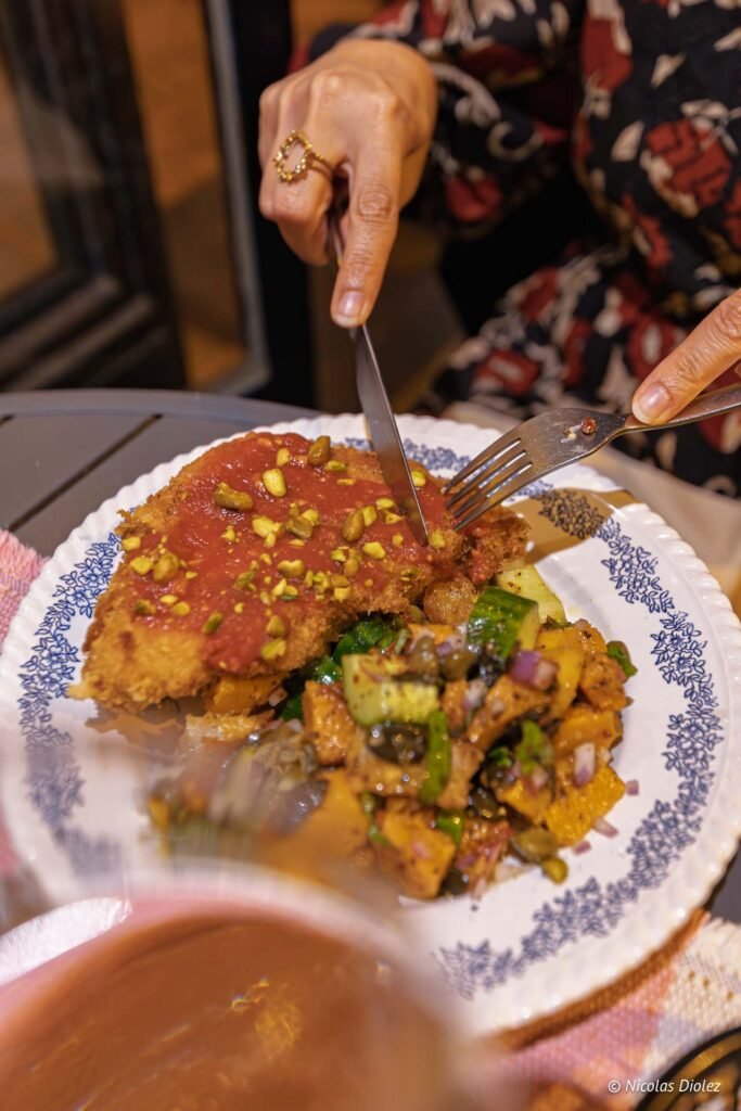 Personne coupant une escalope à la tomate et aux pistaches avec une salade au restaurant La Prohibition, Sète.