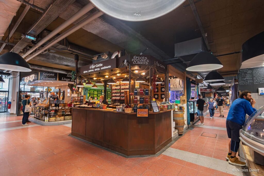Étal d'épices L'Épi-Cette au sein des Halles de Sète avec clients et commerçants.