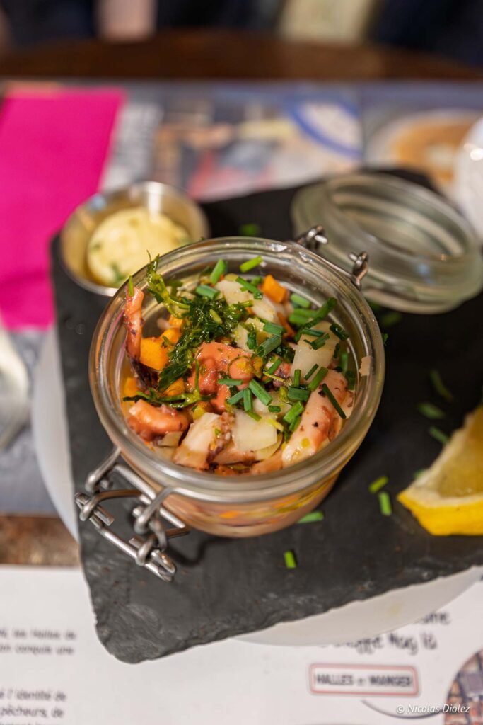 Salade de poulpe servie dans un bocal aux Halles de Sète avec quartier de citron et sauce d'accompagnement.
