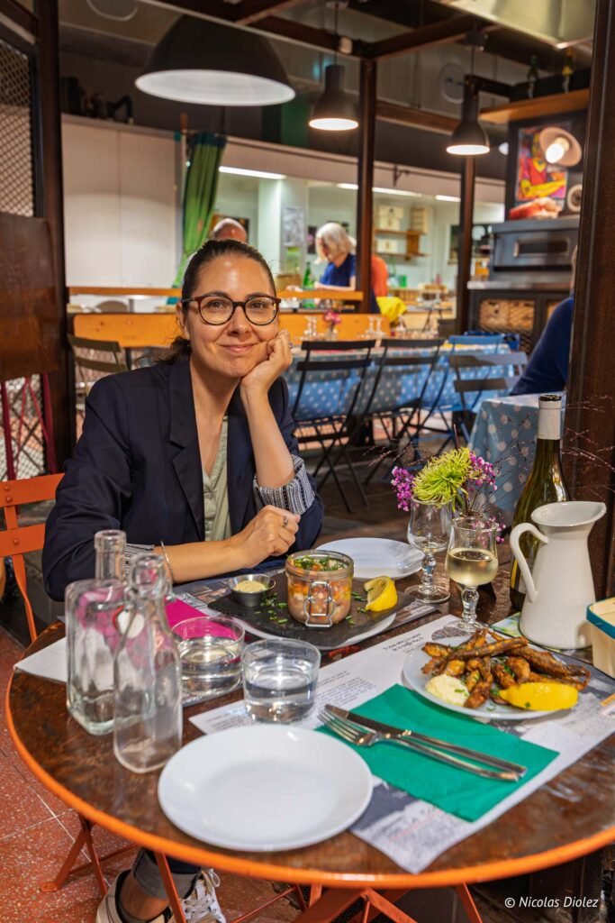 Femme attablée dans les Halles de Sète avec un repas méditerranéen sur une table de restaurant.