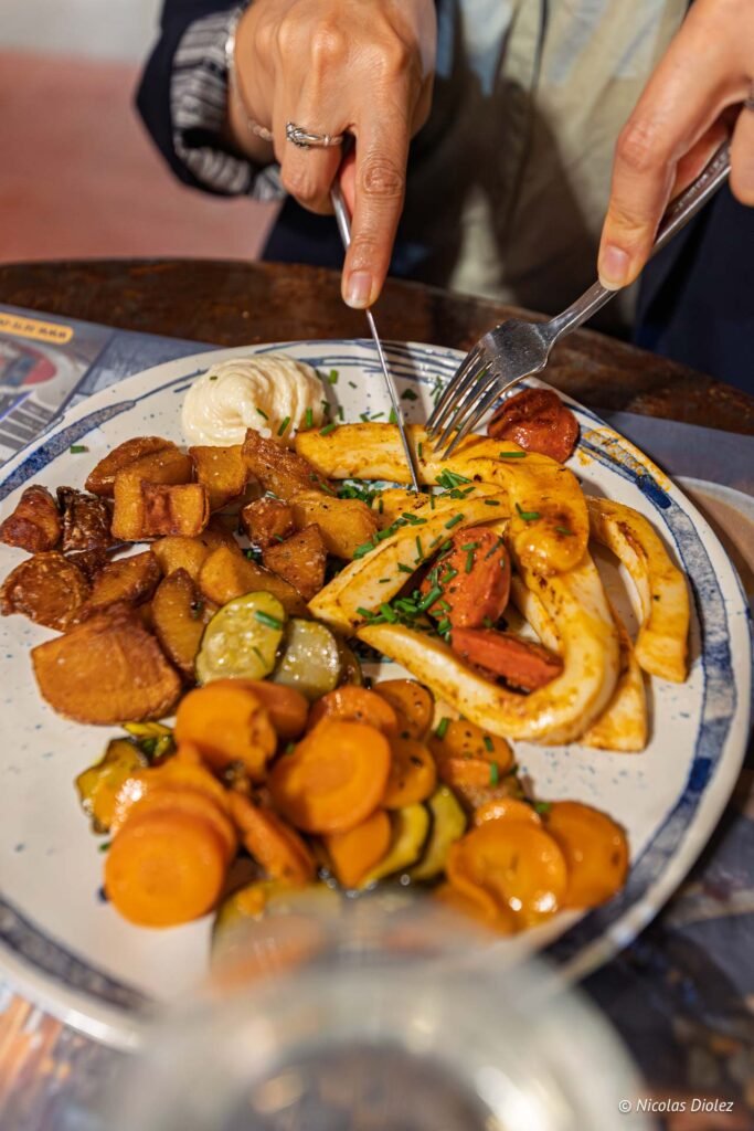 Client coupant des calmars grillés accompagnés de légumes et pommes de terre aux Halles de Sète.
