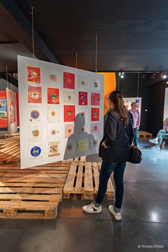 Visiteuse observant une exposition d'étiquettes de fruits vintage suspendues sur des panneaux au musée MIAM de Sète.