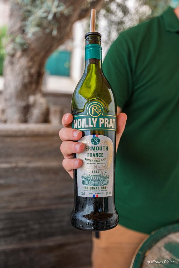 Main tenue à la main, bouteille de vermouth Original Dry Noilly Prat à la Maison Noilly Prat.