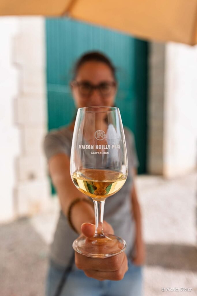 Verre de vermouth Maison Noilly Prat à Marseillan tenu par une femme en arrière-plan flou.