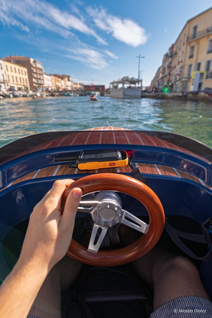Pilote tenant le volant d'un miniboat naviguant dans le canal de Sète, avec une radio Motorola sur le tableau.