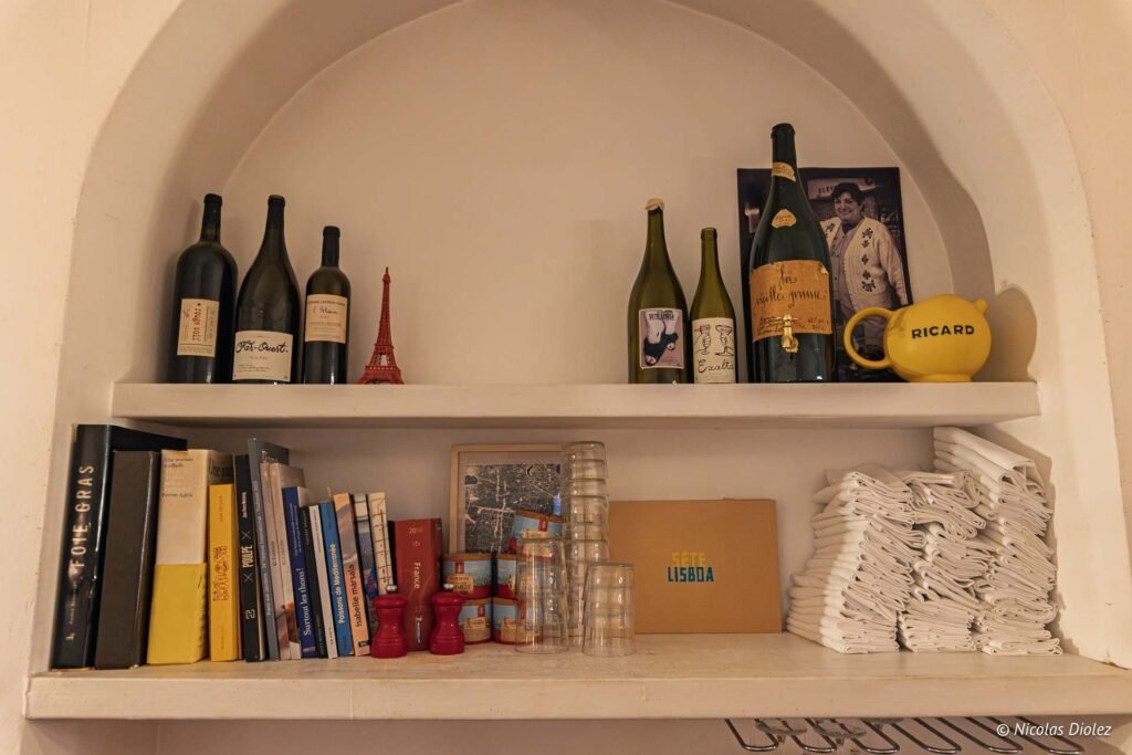 Étagères décorées avec des bouteilles de vin, des livres, des verres et une carafe Ricard au restaurant Paris-Méditerranée Sète.
