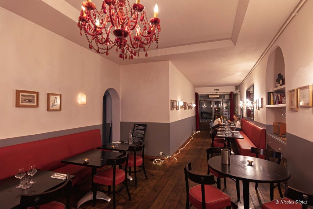 Intérieur du restaurant Paris Méditerranée à Sète avec banquettes rouges et tables en bois, ambiance chaleureuse et lumineuse.