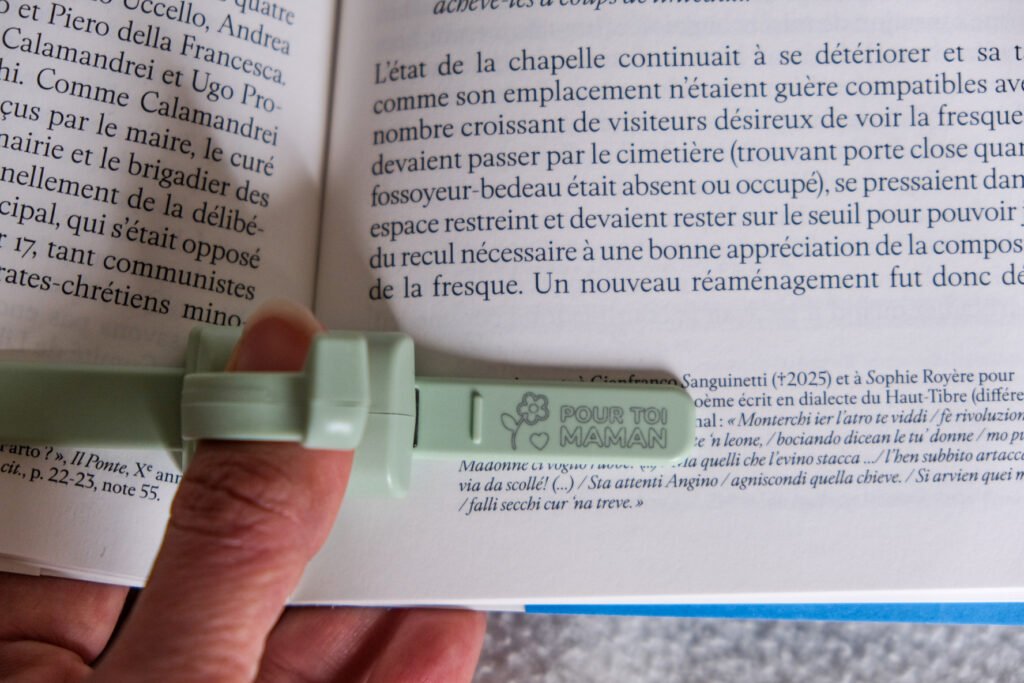 Main qui tient un marque-page vert portant l'inscription Pour toi maman sur les pages d'un livre ouvert.