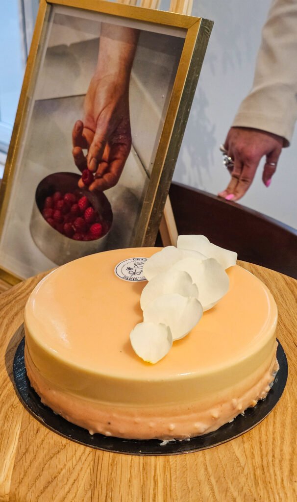 Entremets Graazie Paris glacé à la pêche décoré de pétales blancs, à côté d'une photo encadrée de framboises.