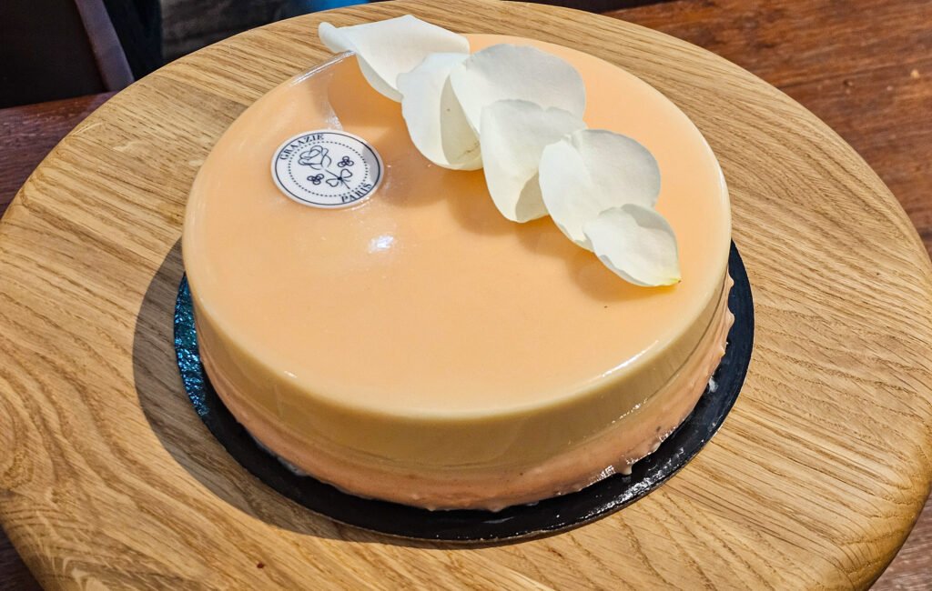 Entremets pâtissier Graazie Paris glacé, décoré de pétales de fleurs blanches sur un support en bois.