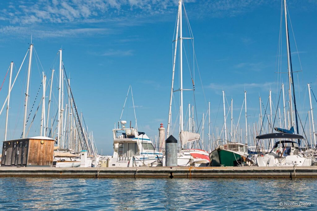 Voiliers et bateaux à moteur amarrés au port de plaisance de Sète avec le phare en arrière-plan.