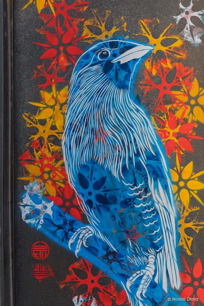 Peinture au pochoir de Nicolas Diolez représentant un oiseau bleu sur fond de motifs floraux stylisés à Sète.