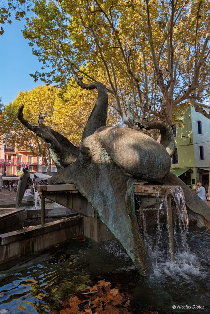 Fontaine sculpture pieuvre sur la place centrale de Sète avec des arbres en automne.