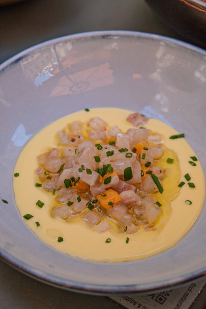 Tartare de poisson cru servi sur une sauce onctueuse avec des herbes fraîches dans une assiette creuse.