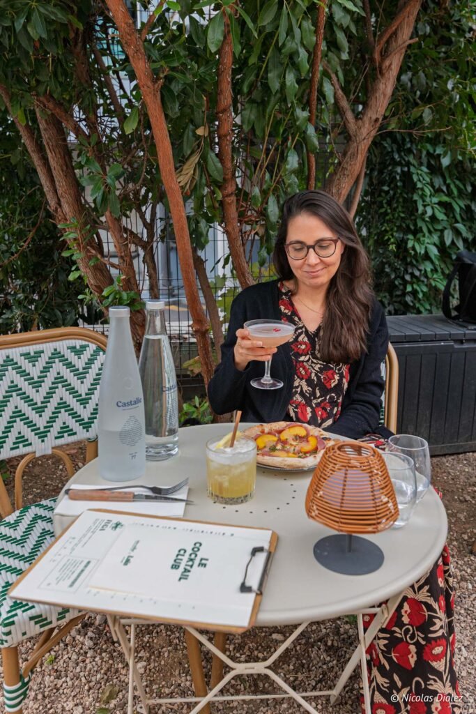Femme dégustant un cocktail Alain Milliat et une pizza à la terrasse du restaurant Laia au Voltaire.