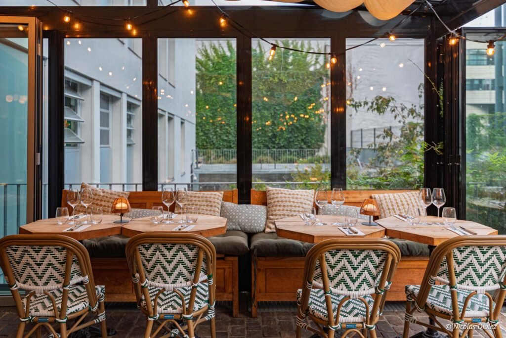 Terrasse couverte du restaurant Laïa Voltaire avec tables en bois, chaises en rotin et guirlandes lumineuses.