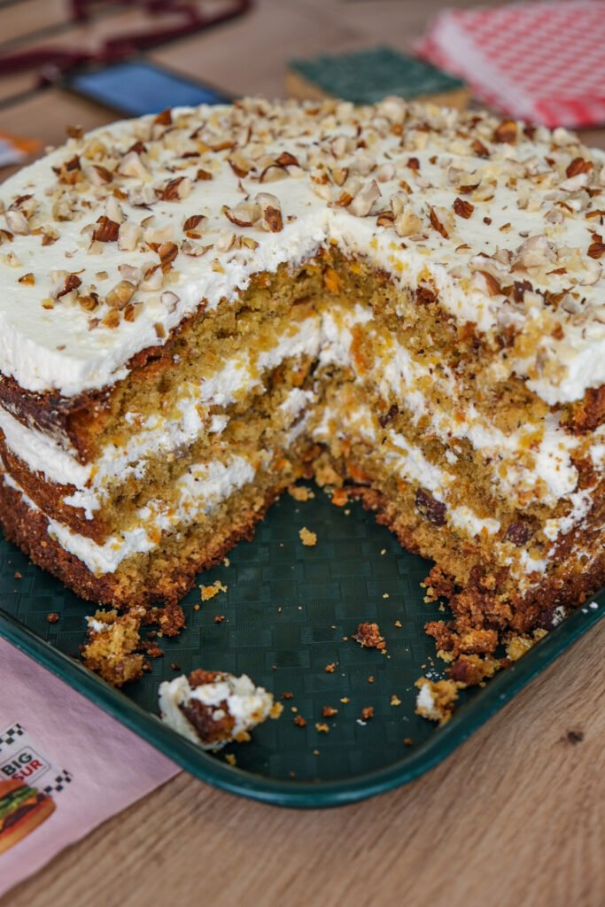 Carrot cake à étages avec glaçage au cream cheese et noix concassées sur un plateau vert.