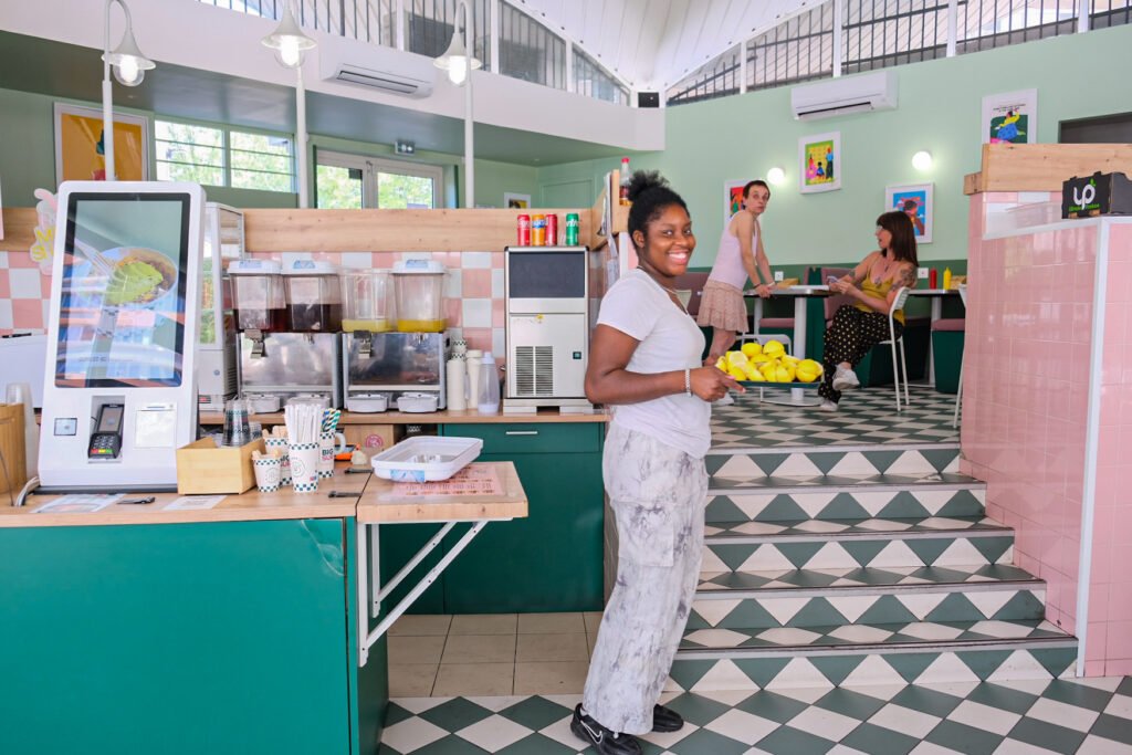 Employée souriante portant un plateau de citrons dans un restaurant Big Sur avec bornes de commande.
