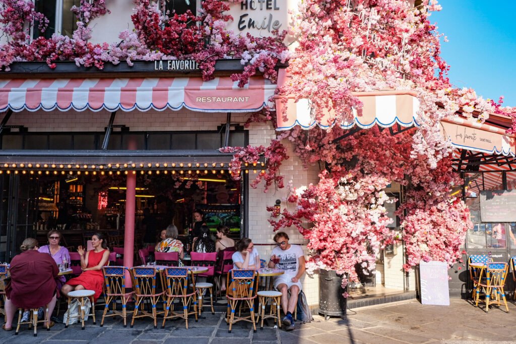 Terrasse du restaurant La Favorite Saint-Paul à Paris décorée de fleurs roses artificielles avec des clients attablés.