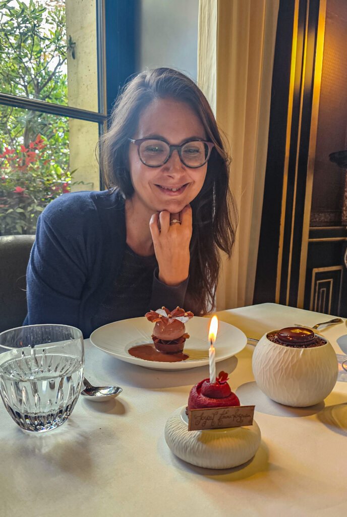 Femme souriante devant un dessert d'anniversaire au restaurant Le Gabriel avec une bougie Joyeux Anniversaire.