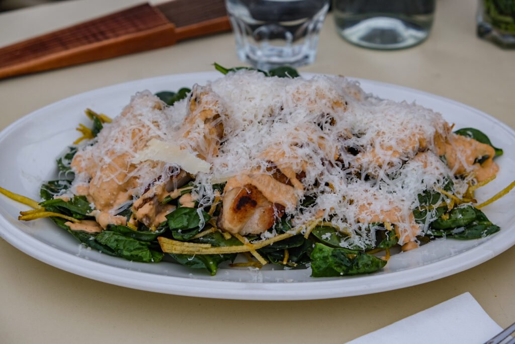 Salade de poulet aux épinards frais, copeaux de parmesan et sauce crémeuse servie dans une assiette blanche.