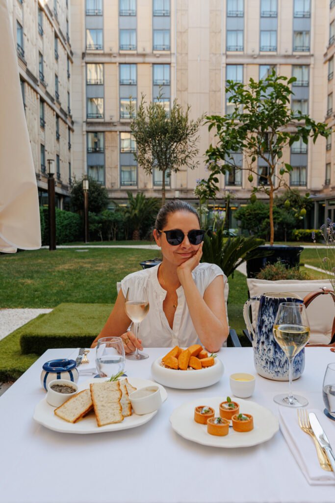 Femme dégustant un repas et du vin sur la terrasse de l'Hôtel Le Collectionneur à Paris.