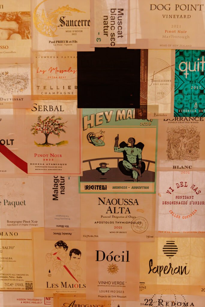 Collage di numerose etichette di bottiglie di vino internazionali provenienti dal ristorante La Petite École a Parigi.