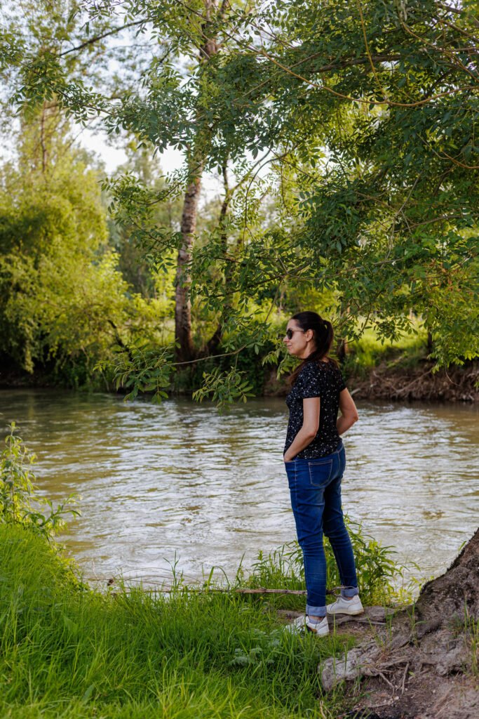 Femme debout au bord d'une rivière en pleine nature, lors d'une balade avec Les Mobylettes de Marinette.
