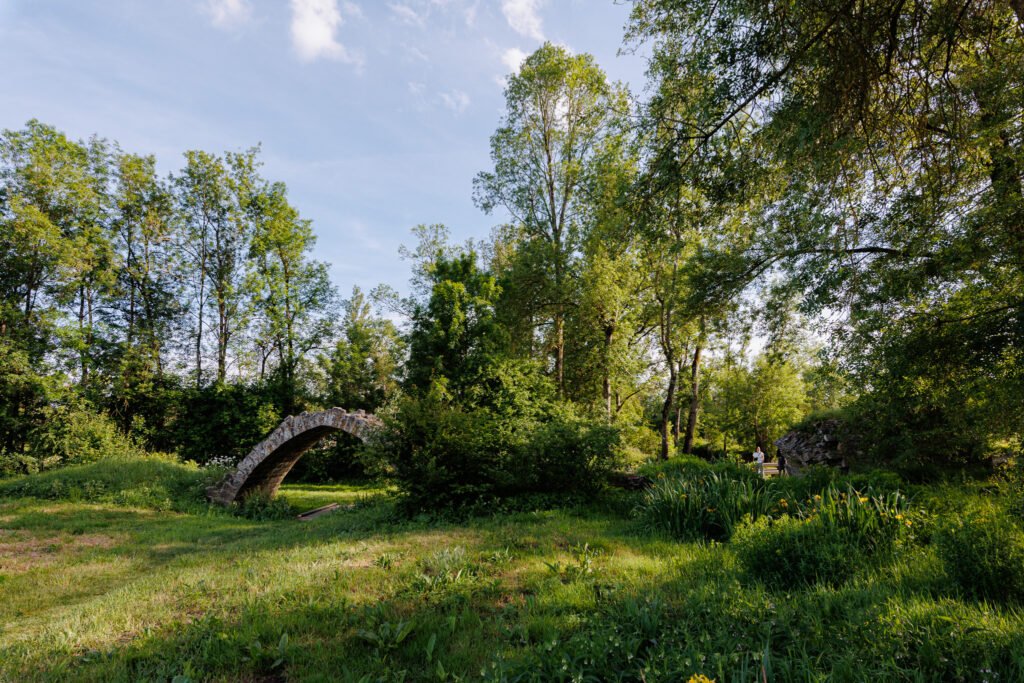 Ancien pont en pierre voûté entouré d'une végétation luxuriante dans un paysage verdoyant lors d'une balade.