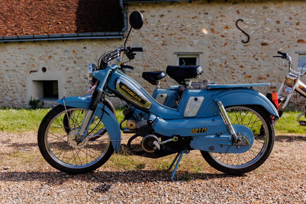 Mobylette Motobécane 881M bleue stationnée devant une ancienne bâtisse en pierre.