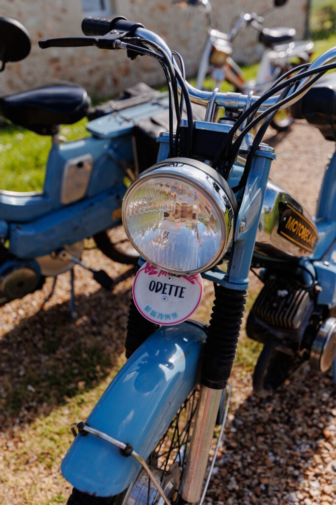 Gros plan sur le phare d'une mobylette bleue Motobécane avec une plaque personnalisée Odette fixée à l'avant.