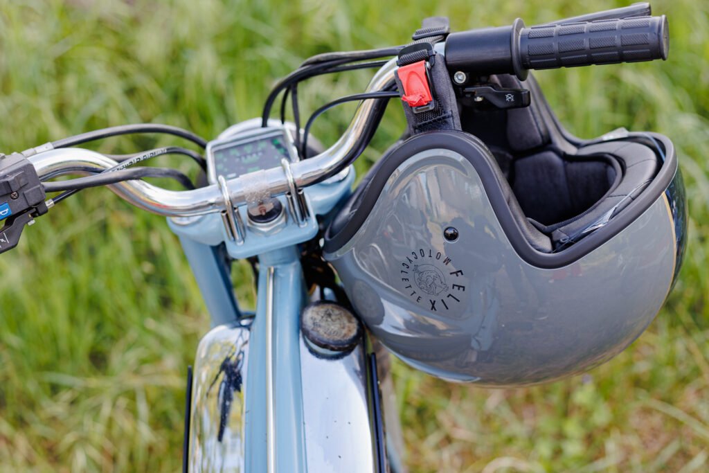 Casque de moto gris avec logo Félix accroché au guidon d'une mobylette vintage.